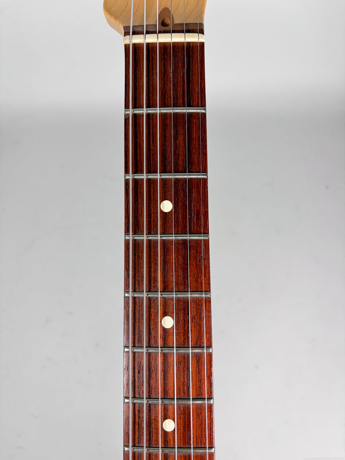 The guitar's dark rosewood fretboard with white dot inlays and metal frets is shown from the nut to the 12th fret.