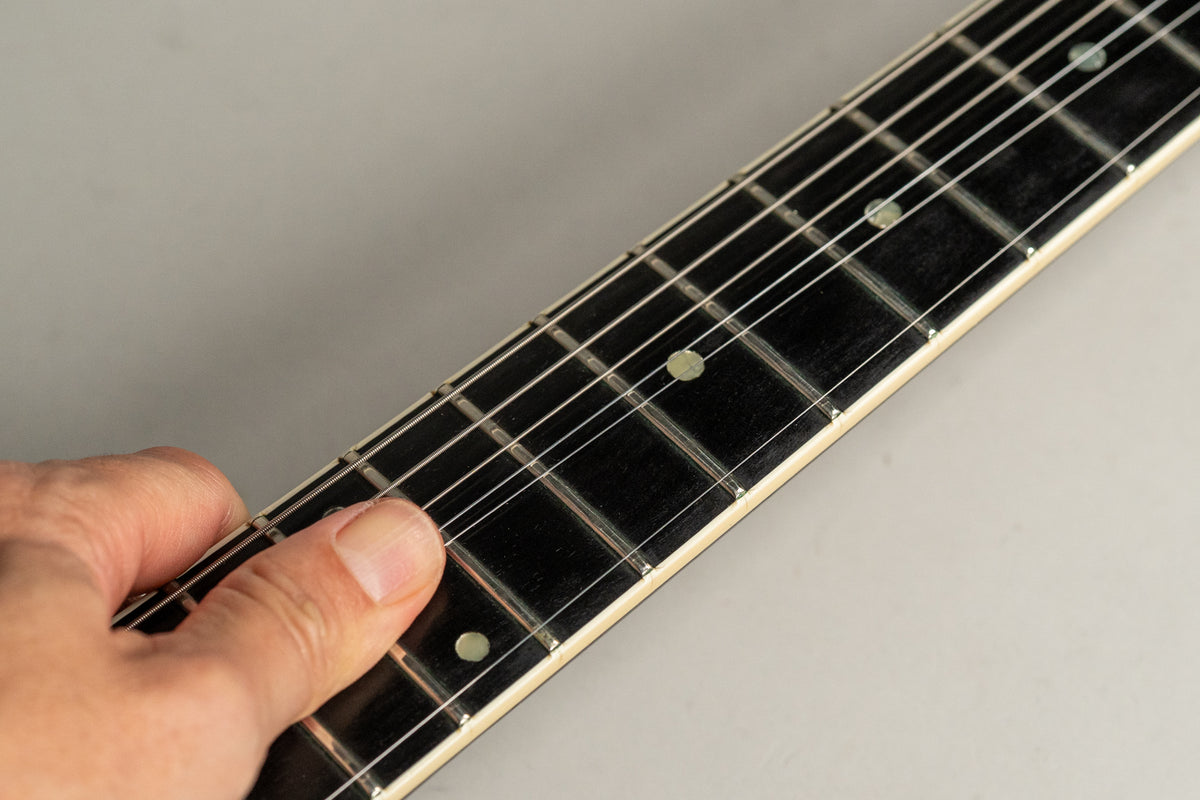 Close-up of a hand fretting the dark rosewood fretboard with dot inlays, showing light wear on the frets.