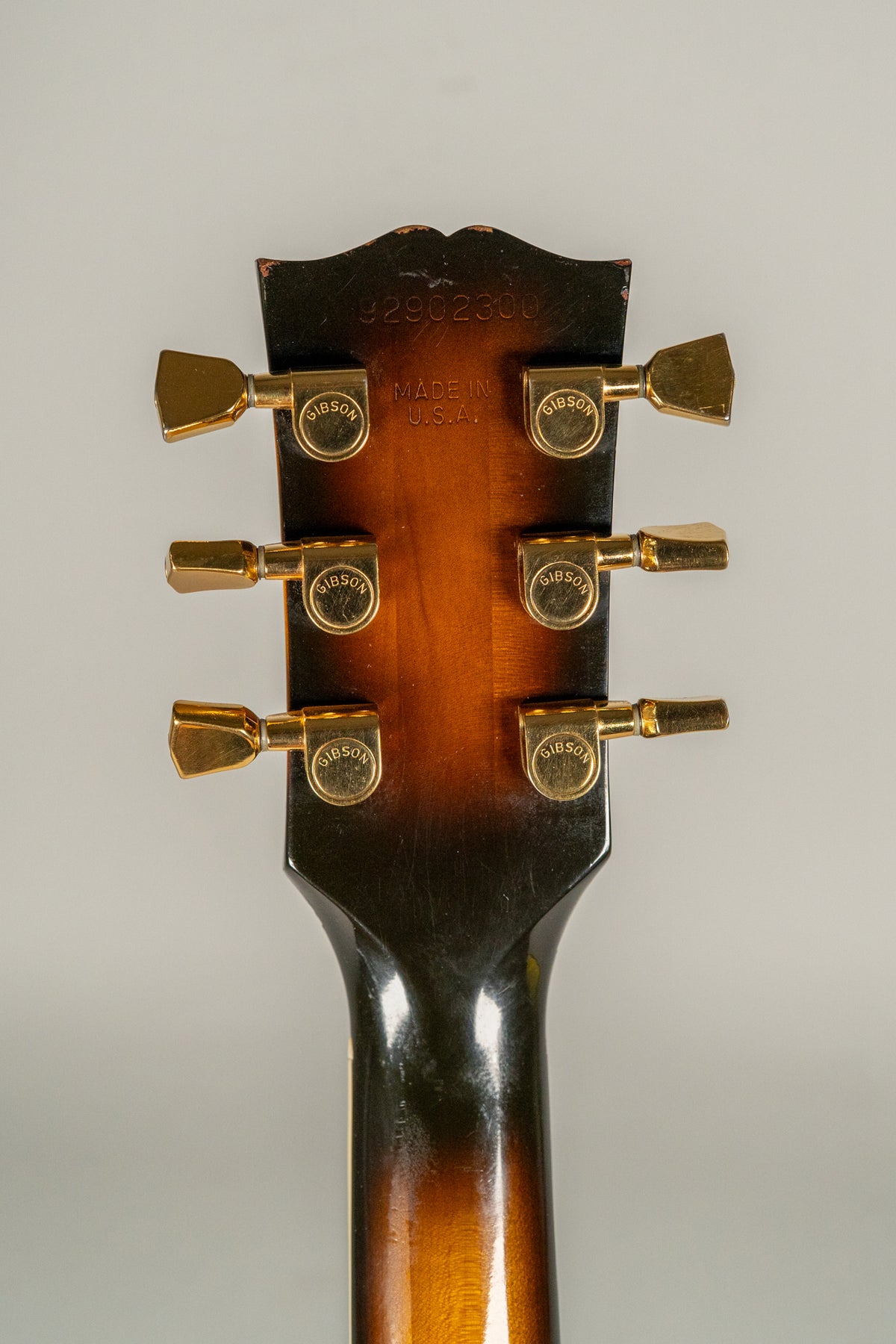 Rear view of the guitar's headstock and upper neck, showing a sunburst finish, six gold tuners, and visible wear on the headstock edges.