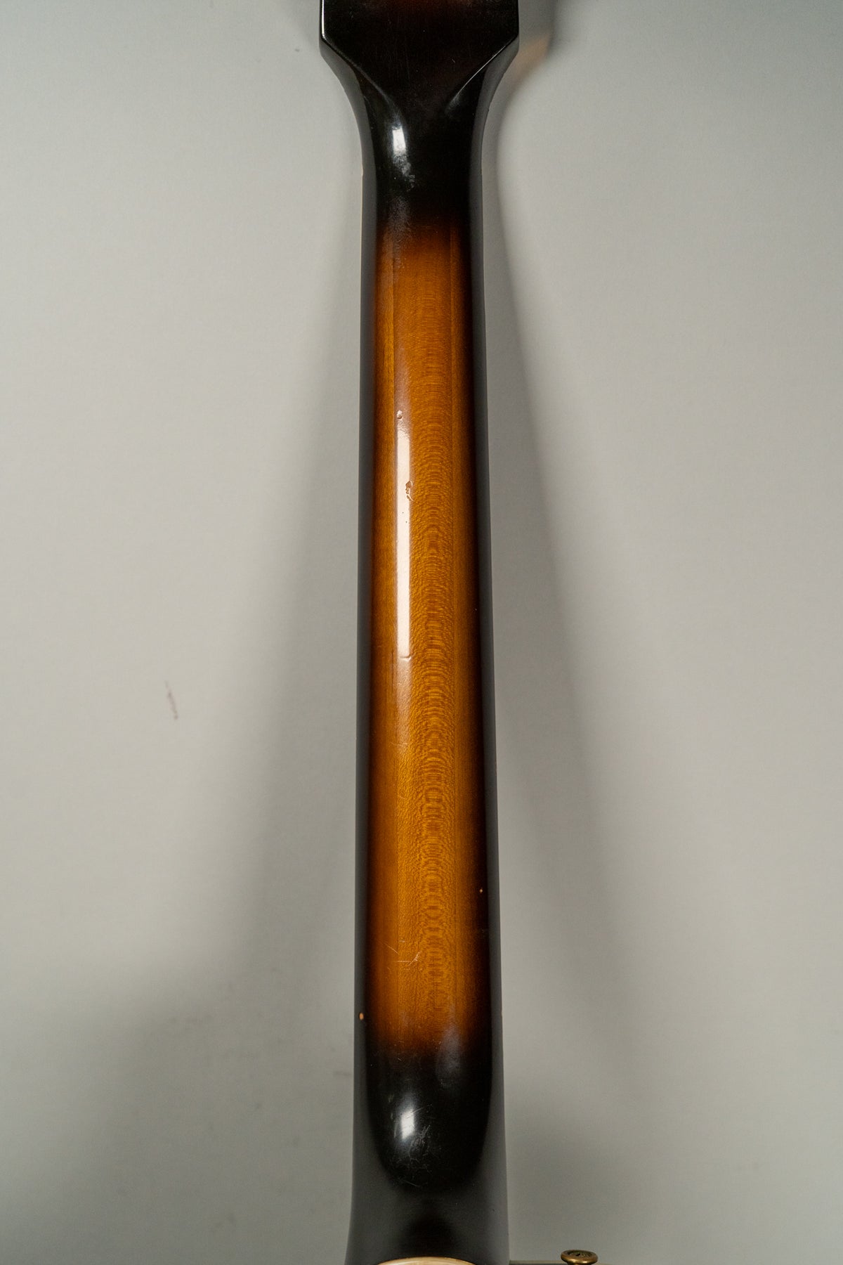 The guitar's neck, viewed from the back, shows a sunburst finish with visible wood grain and some minor dings.