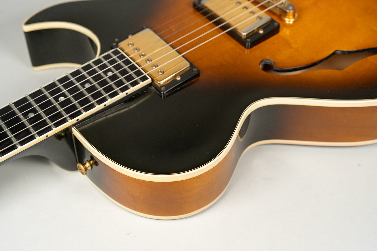 The sunburst archtop guitar's body and neck are framed from above, showing gold hardware and a single lower f-hole.