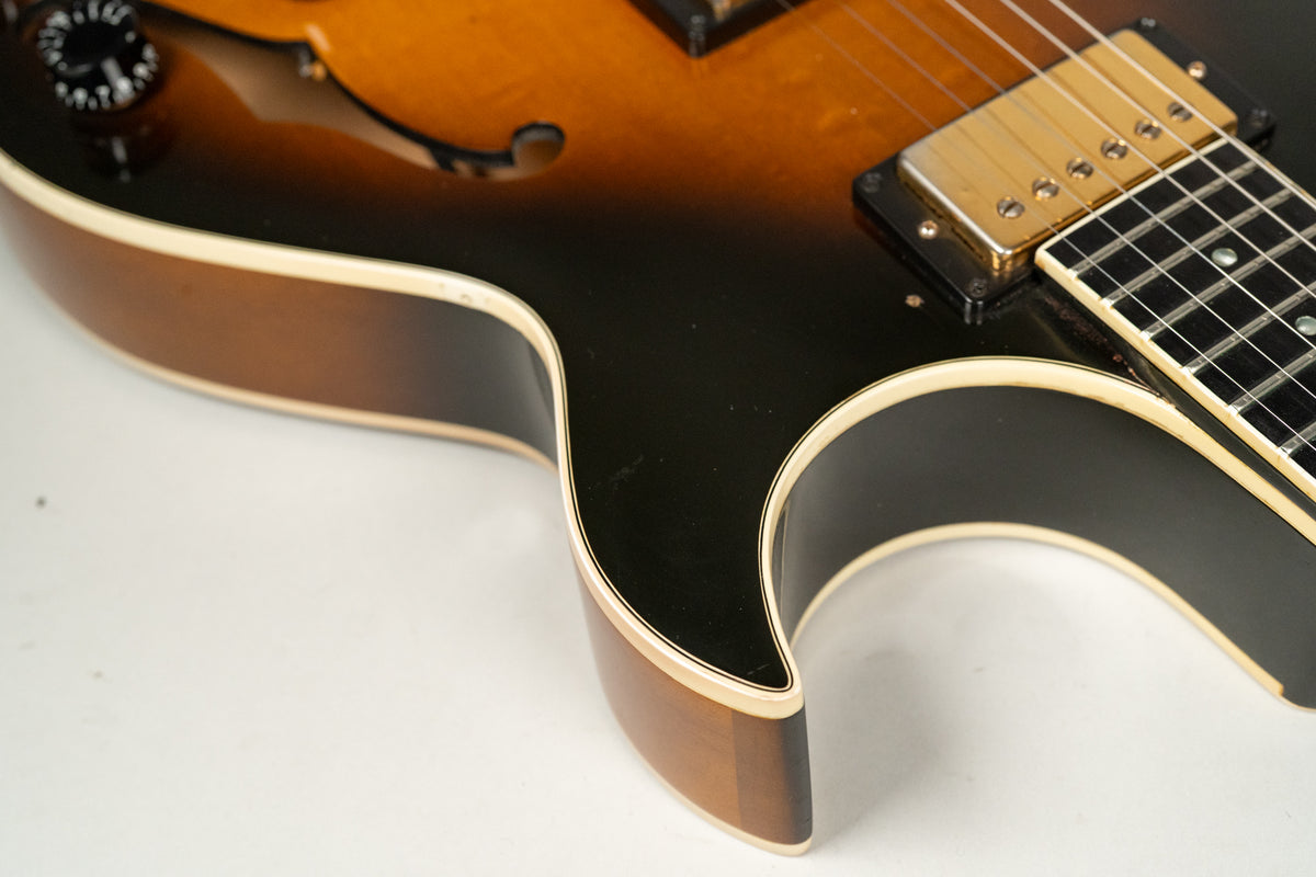 Close-up of the sunburst body's lower bout, showing the f-hole, gold humbucker, and fretboard with binding and light wear.