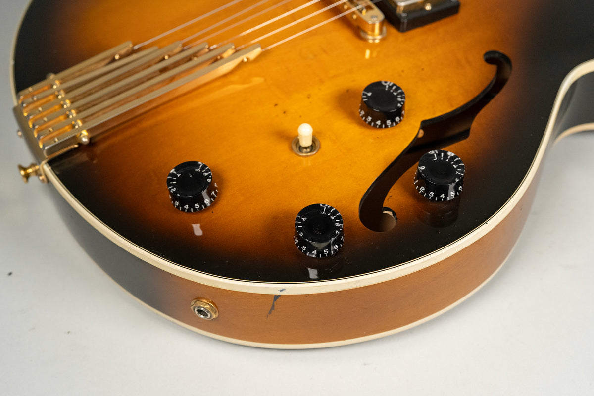 Close-up of the sunburst body, showing four black control knobs, a cream pickup selector, and a gold trapeze tailpiece.