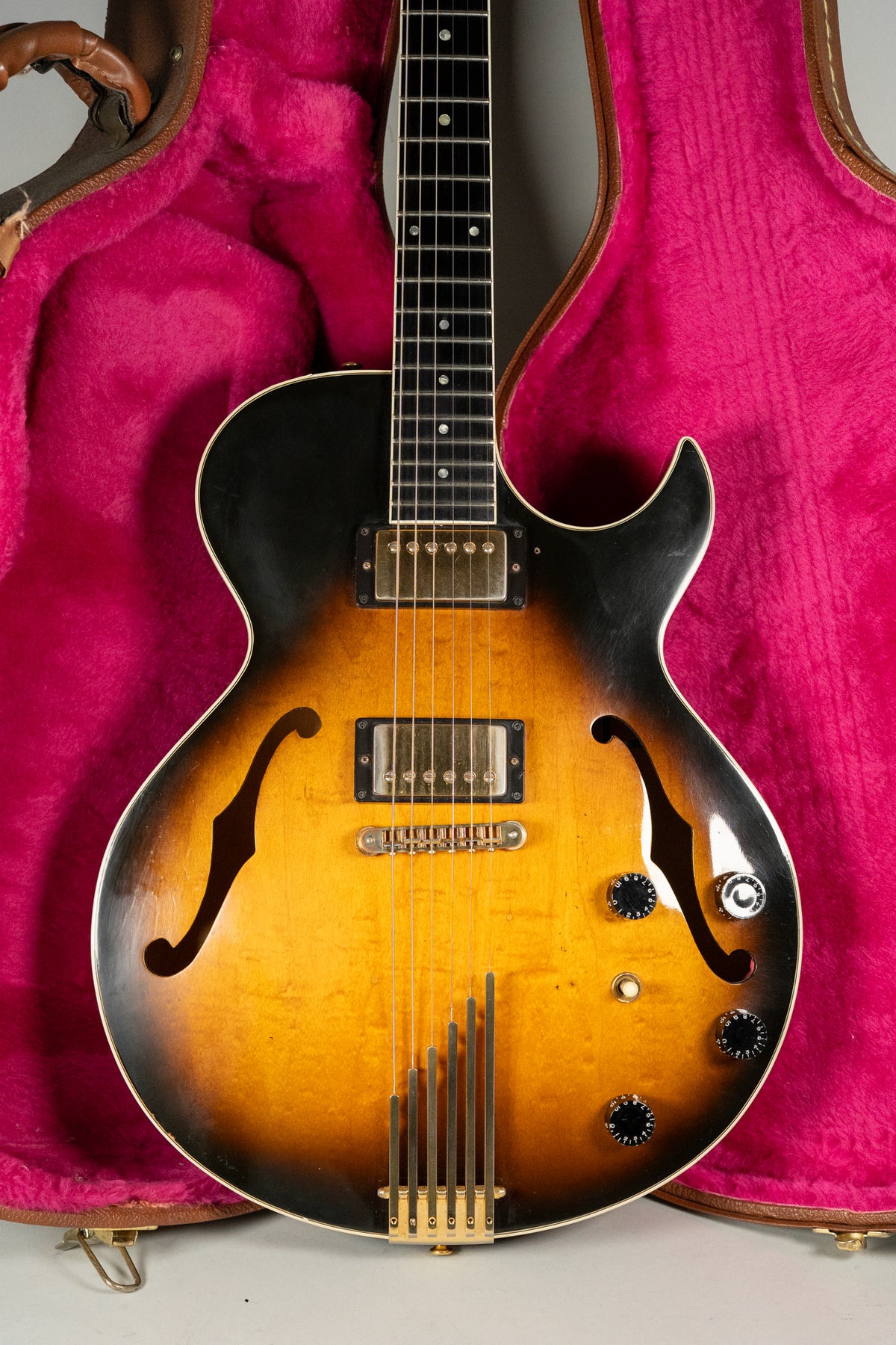 Full-frame shot of a sunburst hollow-body electric guitar with gold hardware, two humbuckers, and four control knobs, in a pink-lined case.