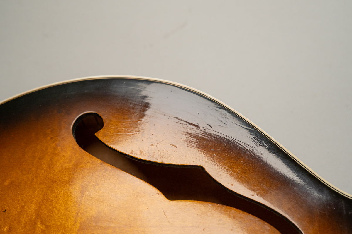 Close-up of the guitar's sunburst body, showing an f-hole and heavy pick wear and scratches on the glossy finish above it.