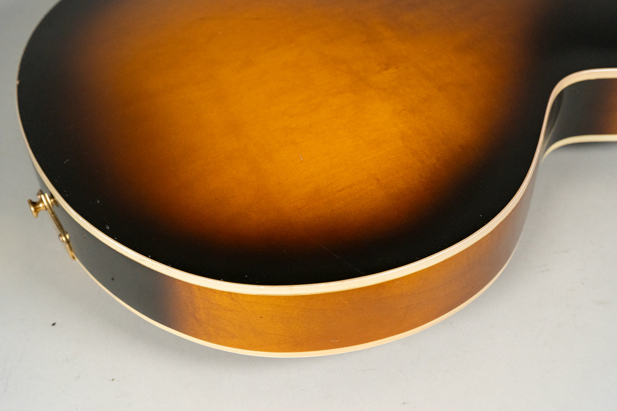 Close-up of the guitar's lower bout, showing the sunburst finish, cream binding, and a gold strap button with minor wear.