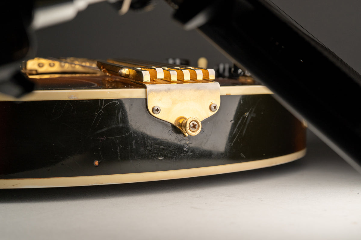 Close-up of the guitar's lower bout, showing the gold tailpiece and strap button, with many scratches on the dark sunburst finish.