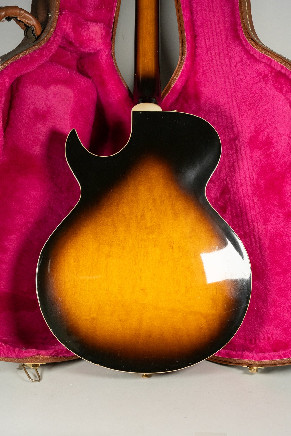 The guitar's sunburst back and neck are visible, with some light scratches, resting in a bright pink plush-lined case.