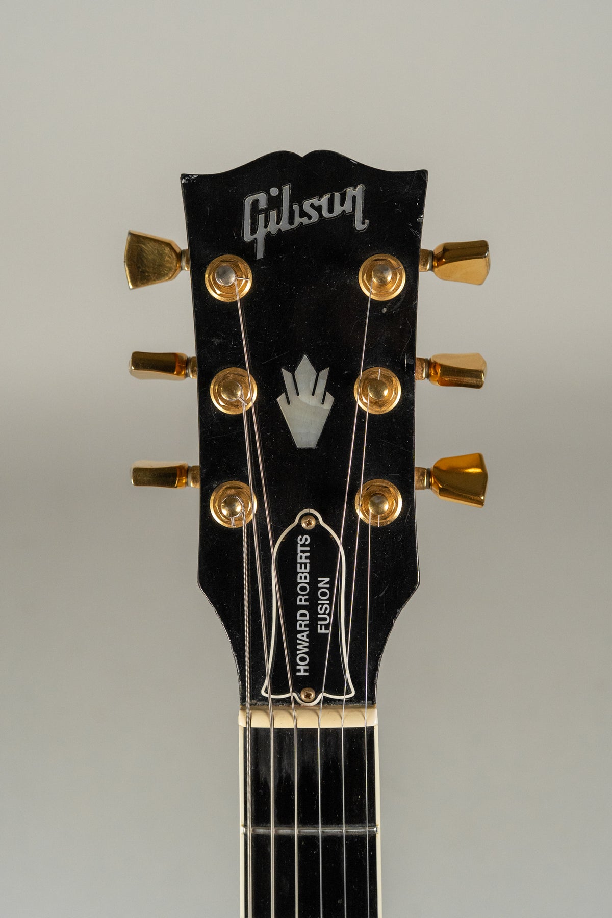 Close-up of the black headstock with gold tuners, showing a mother-of-pearl inlay and some light wear on the finish.
