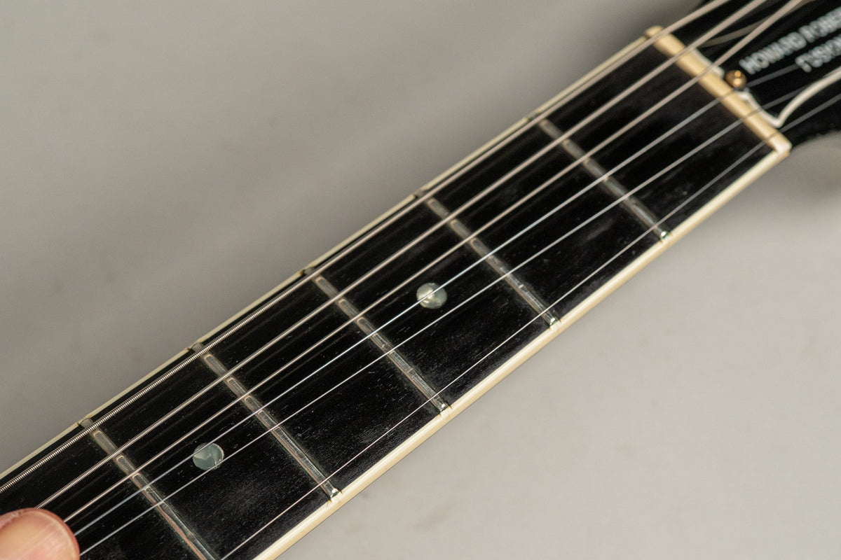 Close-up of the guitar's dark fretboard, showing white binding, metal frets, and circular pearloid inlays.