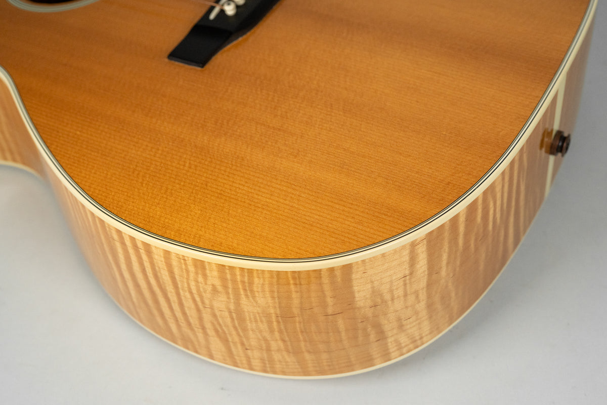 Close-up of the lower bout of a natural finish acoustic guitar, showing the flame maple side and spruce top with binding.