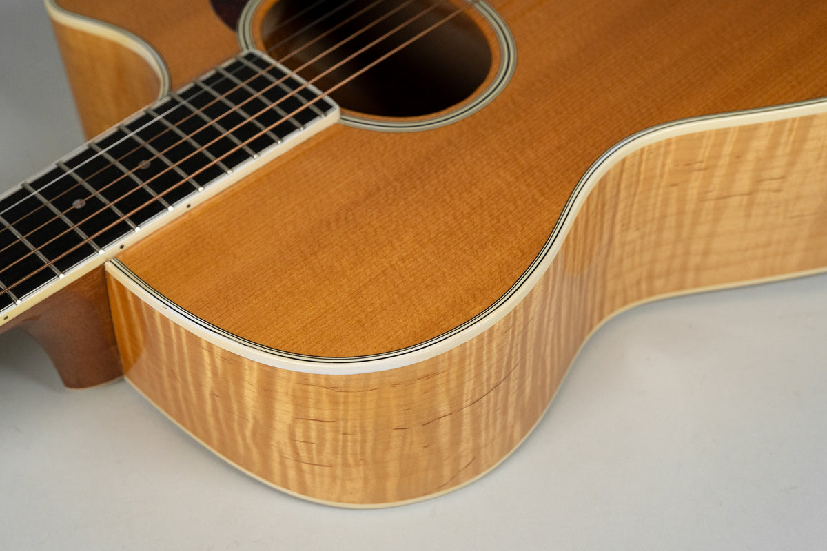 The upper bout and cutaway of a natural finish acoustic guitar, showing the flame maple side and spruce top.