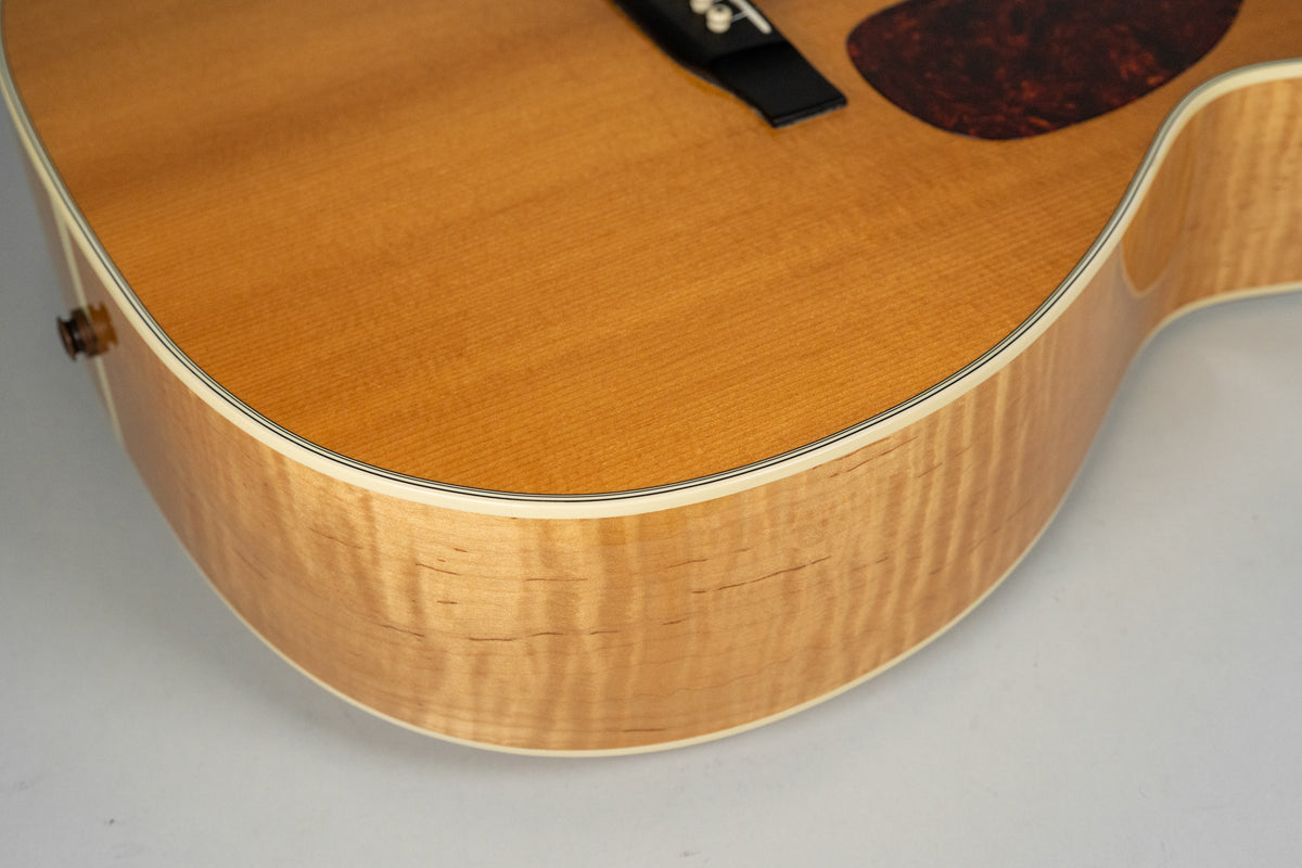 Close-up of the lower bout of a natural finish acoustic guitar, showing the flame maple side and a small portion of the spruce top.