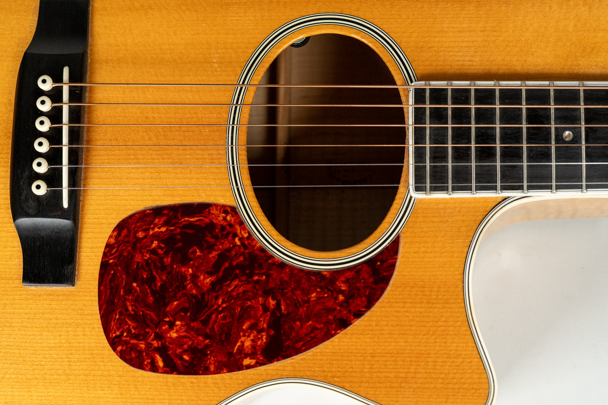 Close-up of the natural finish flame maple body, showing the soundhole with striped rosette, tortoise pickguard, and bridge.