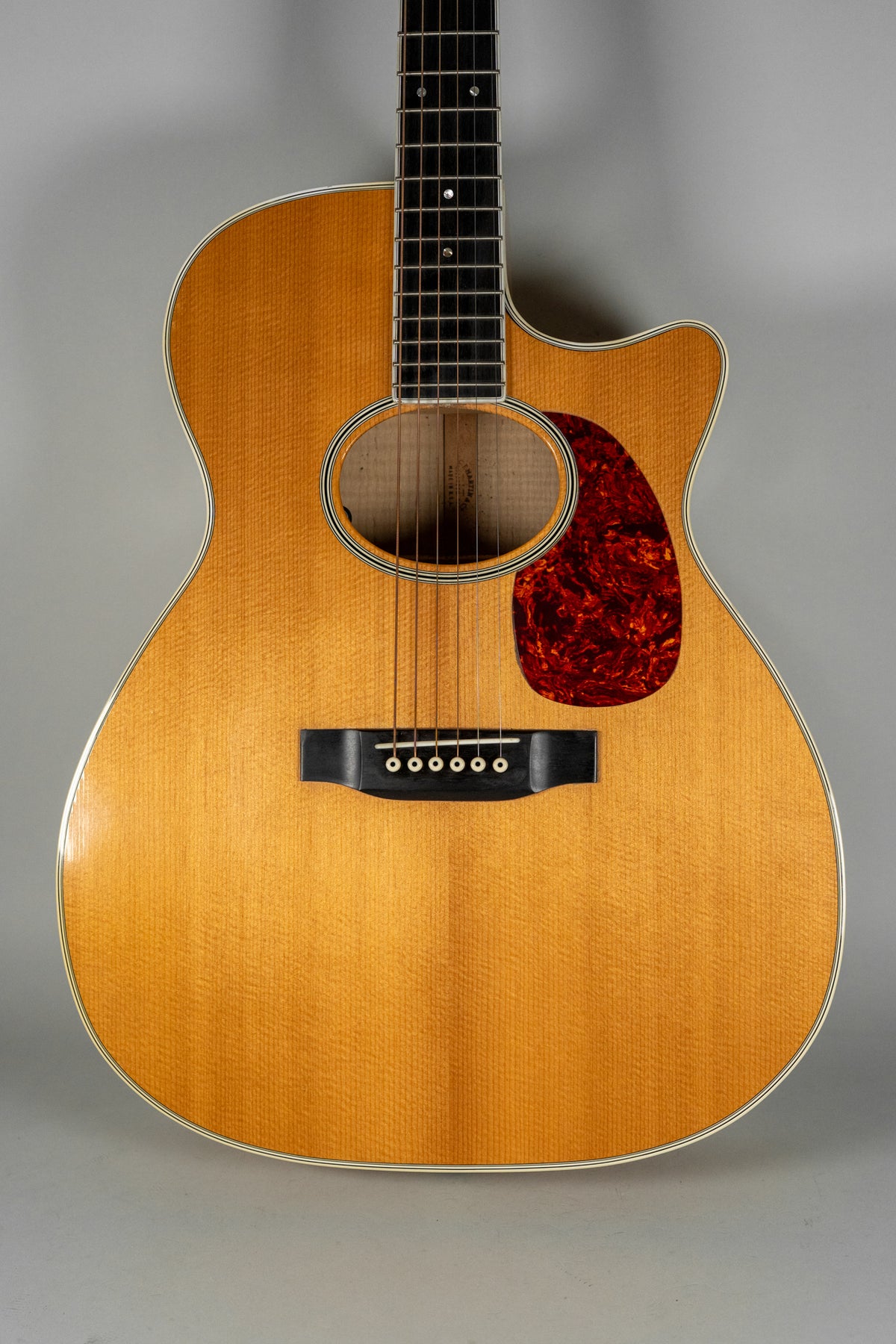 The natural finish acoustic guitar is framed from the neck to the lower bout, showing a cutaway and a tortoiseshell pickguard.