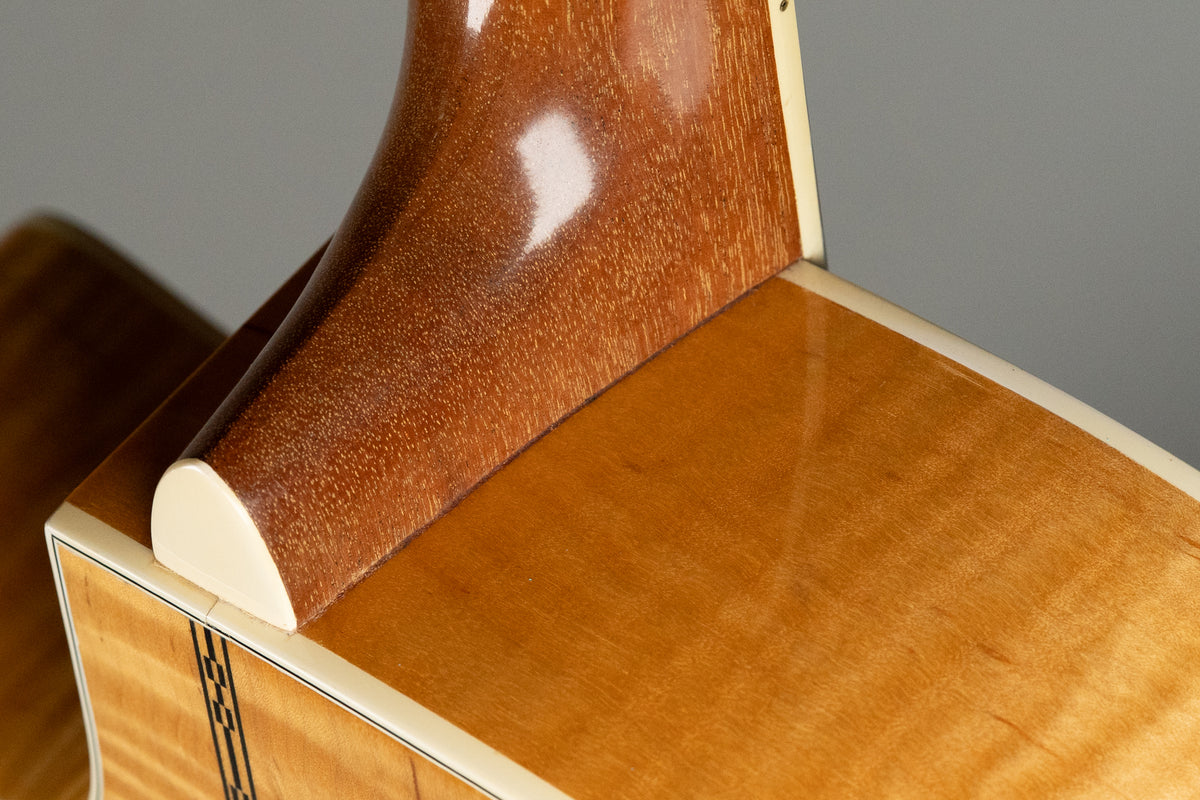 Close-up of the guitar's heel and lower bout, showing the natural flame maple finish, cream binding, and dark wood purfling.
