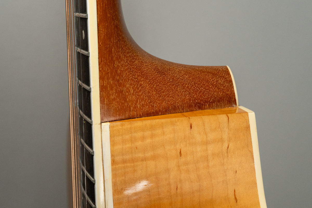 Close-up of the guitar's neck heel and upper body, showing the light natural flame maple finish and dark brown neck.