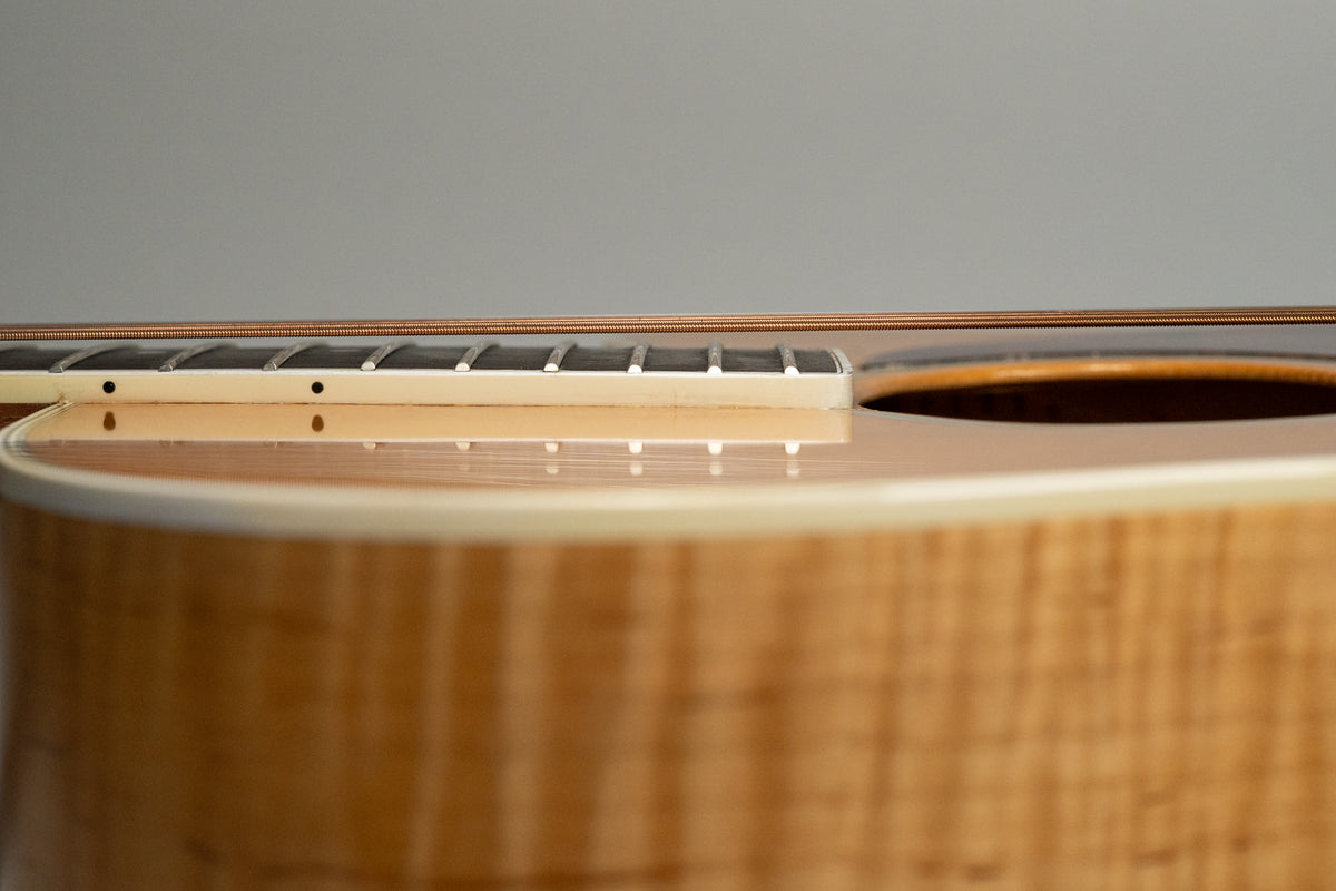 Close-up of the natural flame maple body and soundhole, with the fretboard and strings visible from the side.