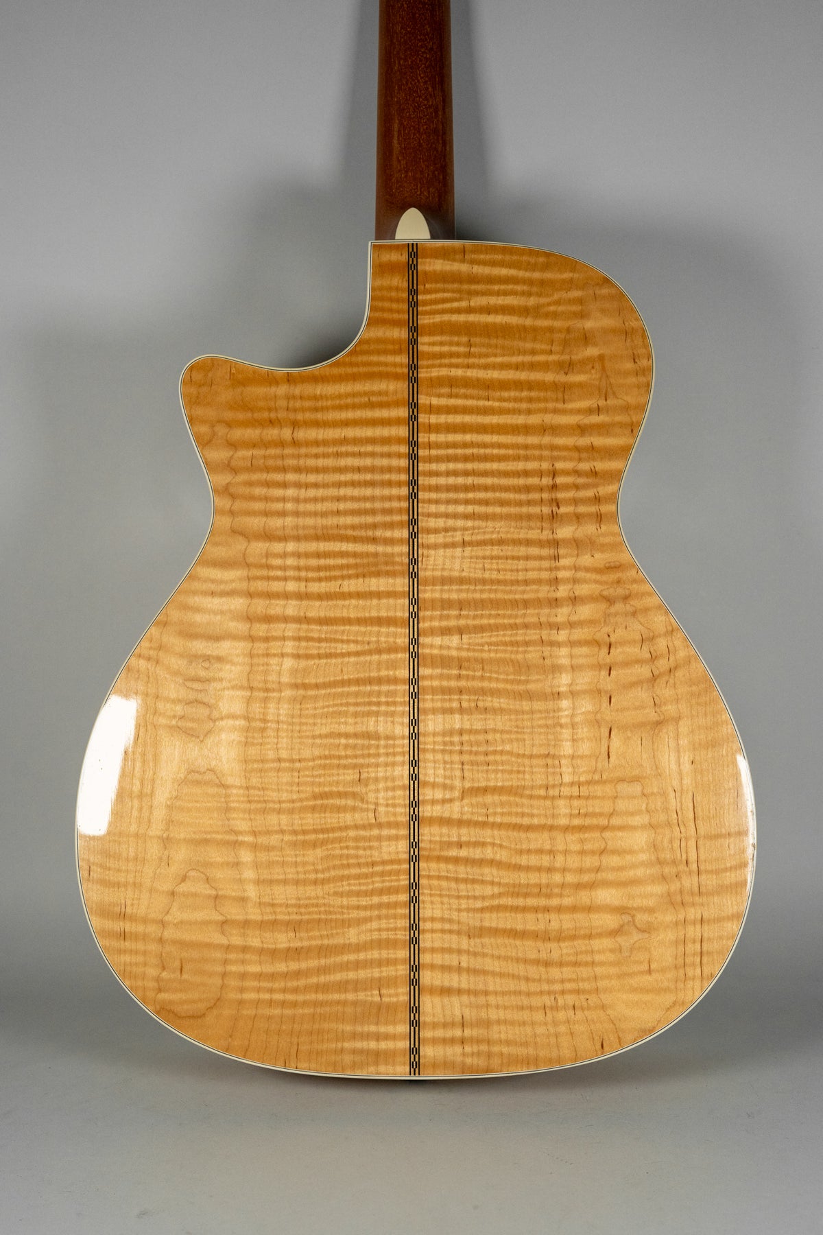 The back of a natural finish flame maple acoustic guitar with a cutaway, showing a dark wood neck and a decorative center strip.