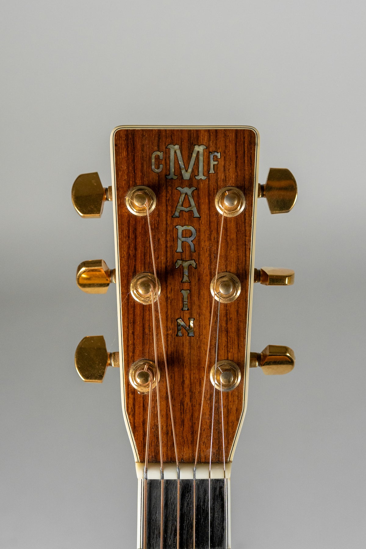 Close-up of the guitar's headstock, showing a dark wood grain with mother-of-pearl inlay and six gold tuning pegs.