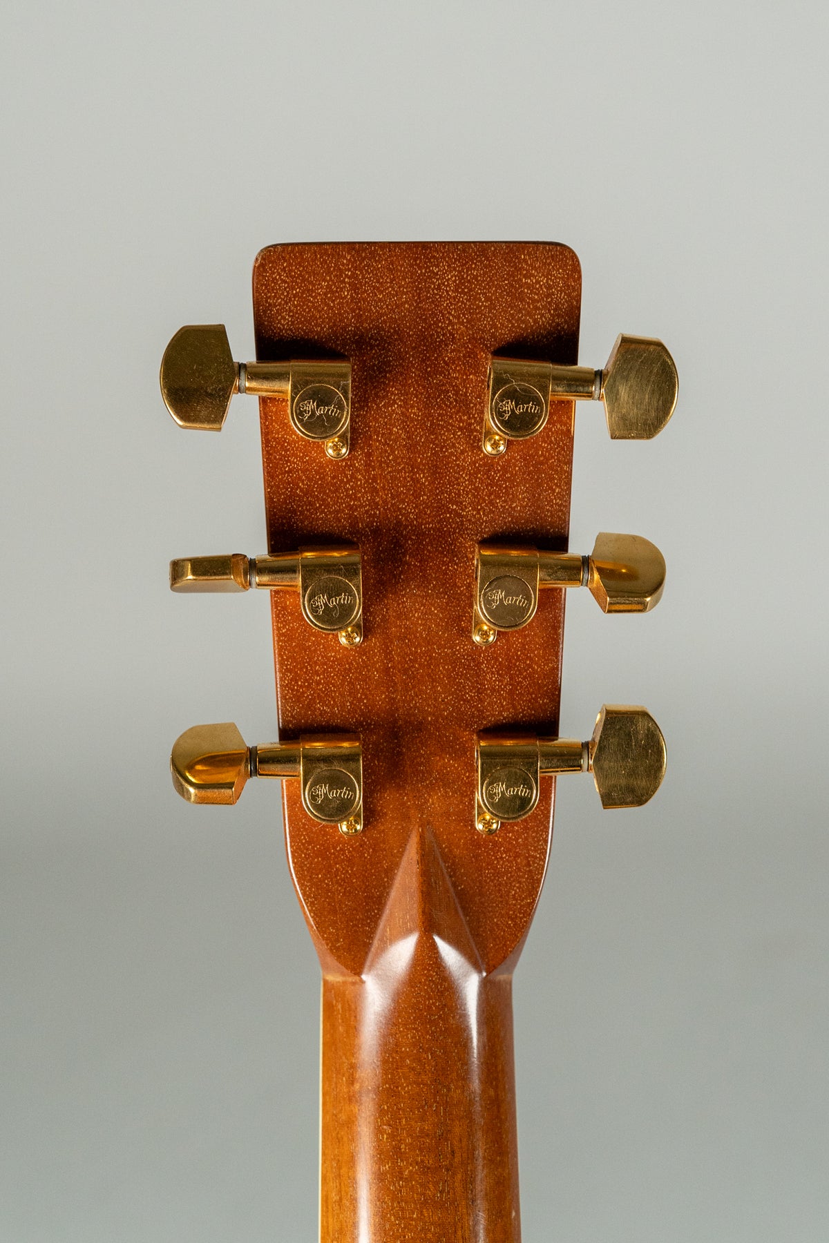 The back of the guitar's headstock and upper neck, showing six gold tuners on a rich brown, glossy finish.