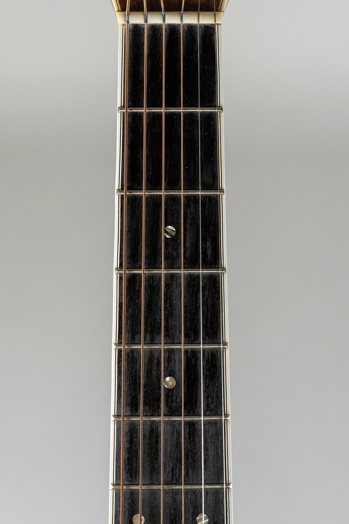 Close-up of the guitar's dark fretboard with light strings, showing circular fret markers at the 5th, 7th, and 9th frets.
