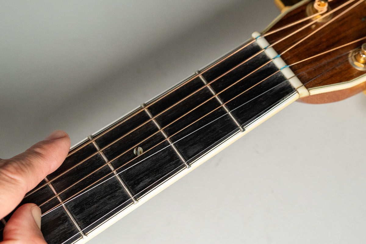 Close-up of the guitar's dark fretboard and nut, with a hand holding down the strings near the first fret.