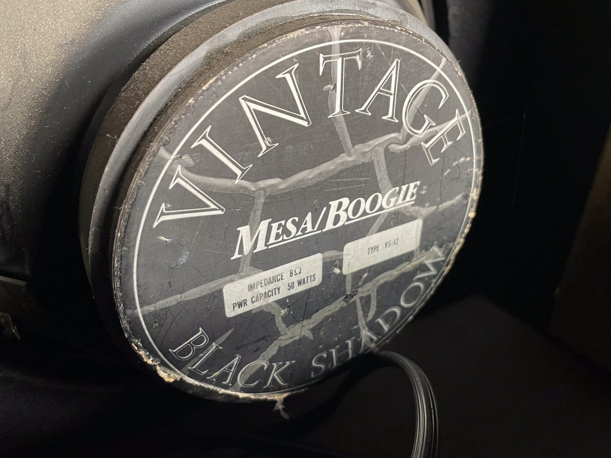 Close-up of the black speaker magnet, showing a worn, cracked label with white text and some dust and debris.