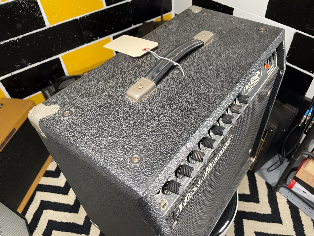Top-down view of a black textured combo amp with a top handle, metal corner protectors, and a row of black control knobs.