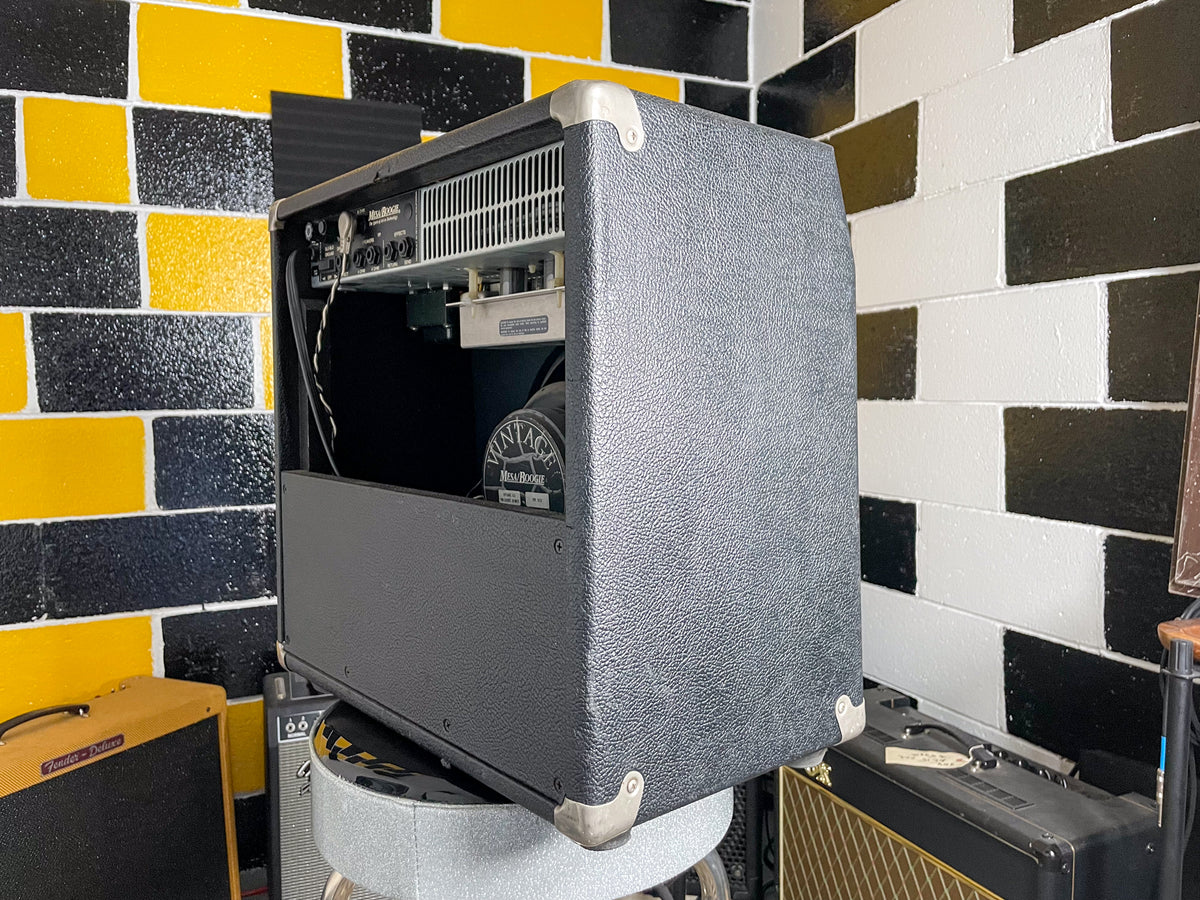 Rear-right view of the black textured combo amp, showing the exposed metal chassis, rear panel jacks, and speaker.