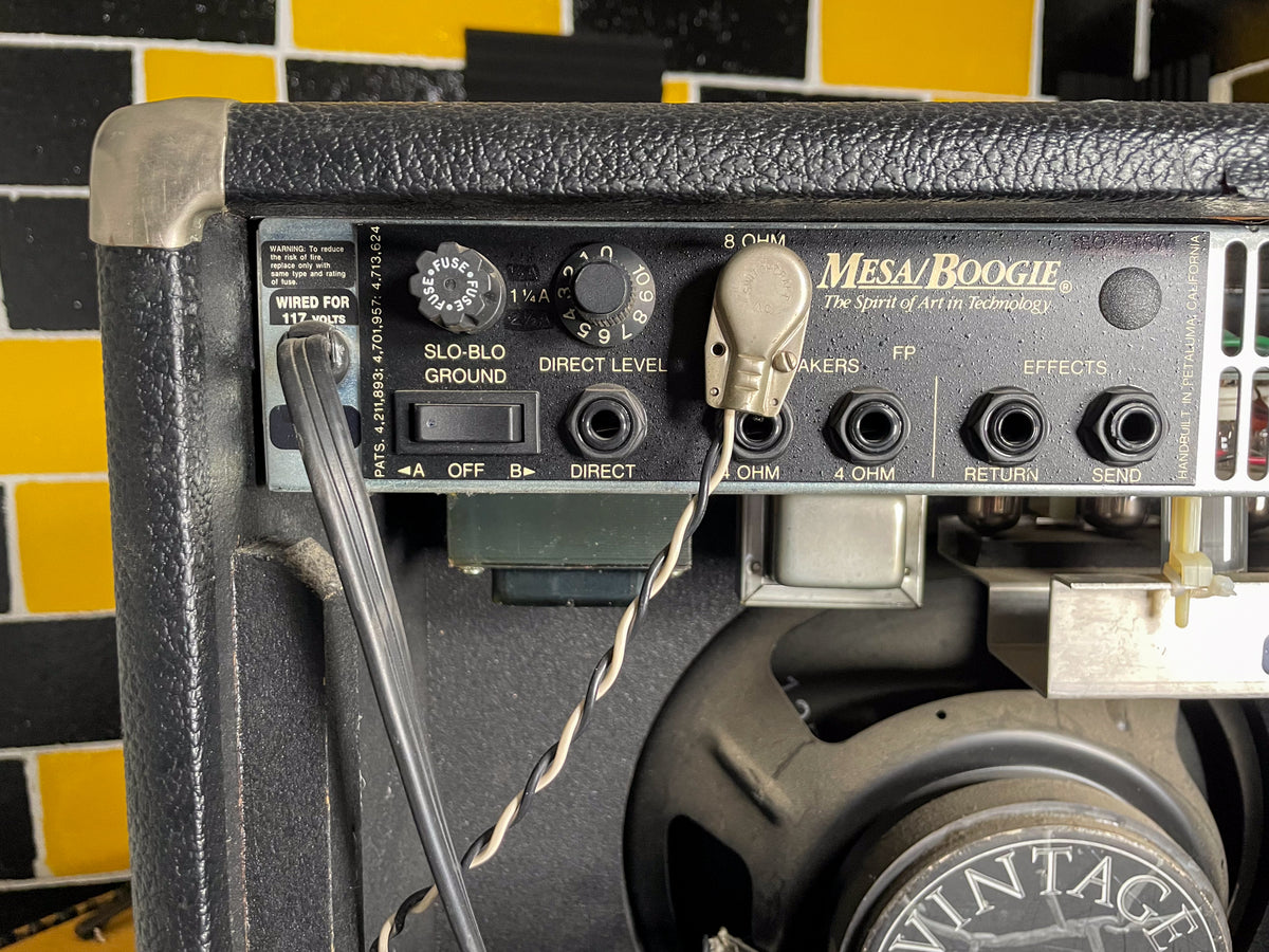 Rear view of the black textured amp, showing the control panel with various jacks, switches, and a fuse, plus a speaker.