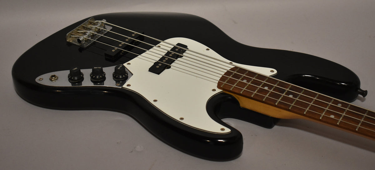 Black Jazz Bass, angled from above, showing the upper body, white pickguard, two black pickups, chrome bridge, and three control knobs.