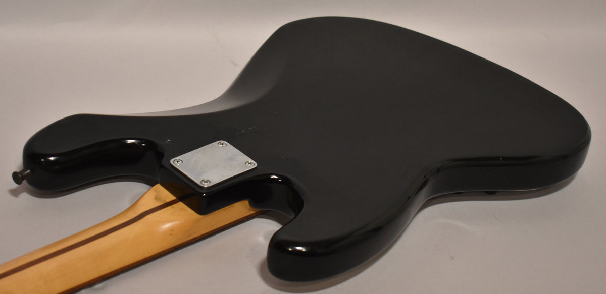 The black bass body, viewed from the back, shows a light maple neck, a four-bolt neck plate, and minor scuffs on the finish.