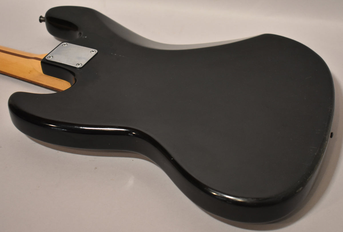 The black bass guitar's back is shown at an angle, revealing a chrome neck plate, a few small dings, and light surface scratches.