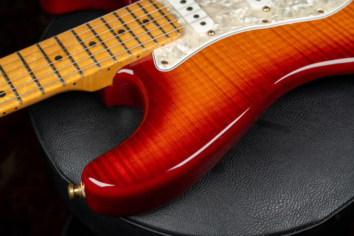 Close-up of the guitar's lower bout, showing a vibrant cherry sunburst flame top, pearloid pickguard, and maple fretboard.