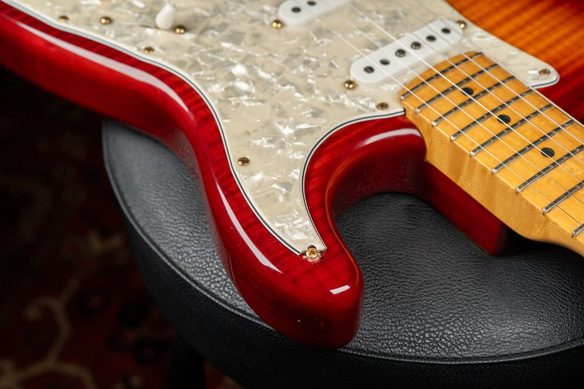 Close-up of the guitar's lower bout, showing the glossy cherry sunburst finish, pearloid pickguard, and maple fretboard.