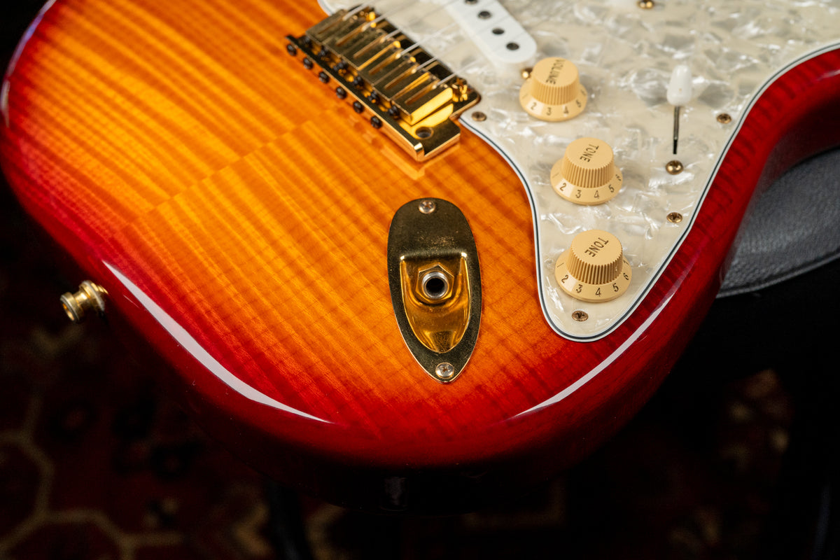 The lower bout of a sunburst flame top guitar, showing gold hardware, pearloid pickguard, and three cream control knobs.