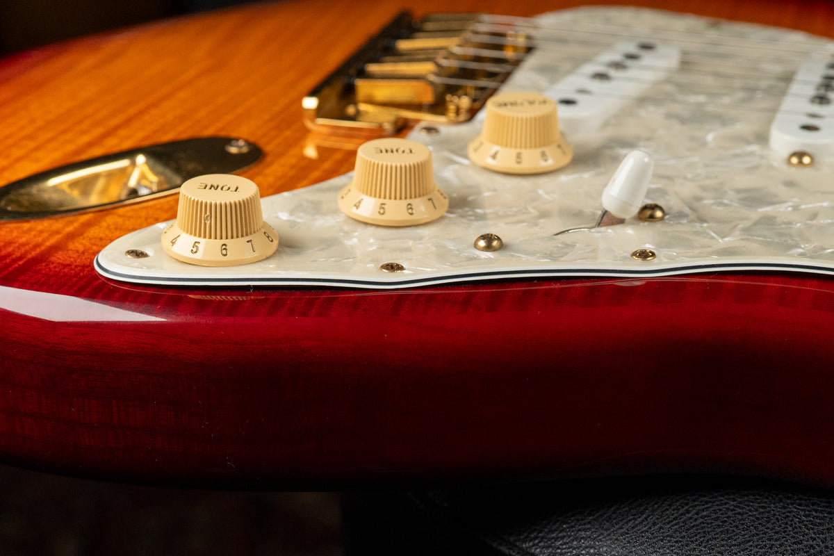 Close-up of the guitar's lower body, showing a red-to-orange sunburst finish, pearloid pickguard, and three cream control knobs.