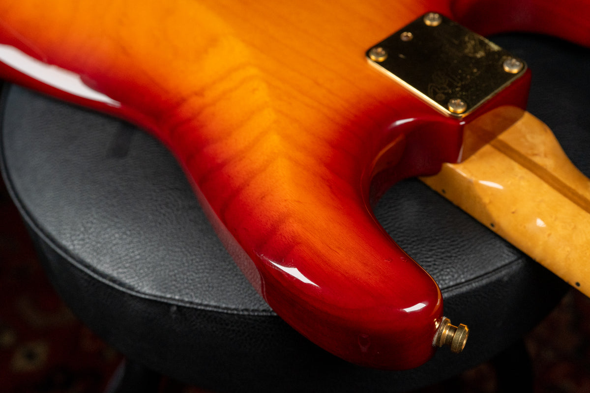 Close-up of the guitar's lower bout and neck heel, showing a glossy cherry sunburst finish with flame maple grain and a gold neck plate.