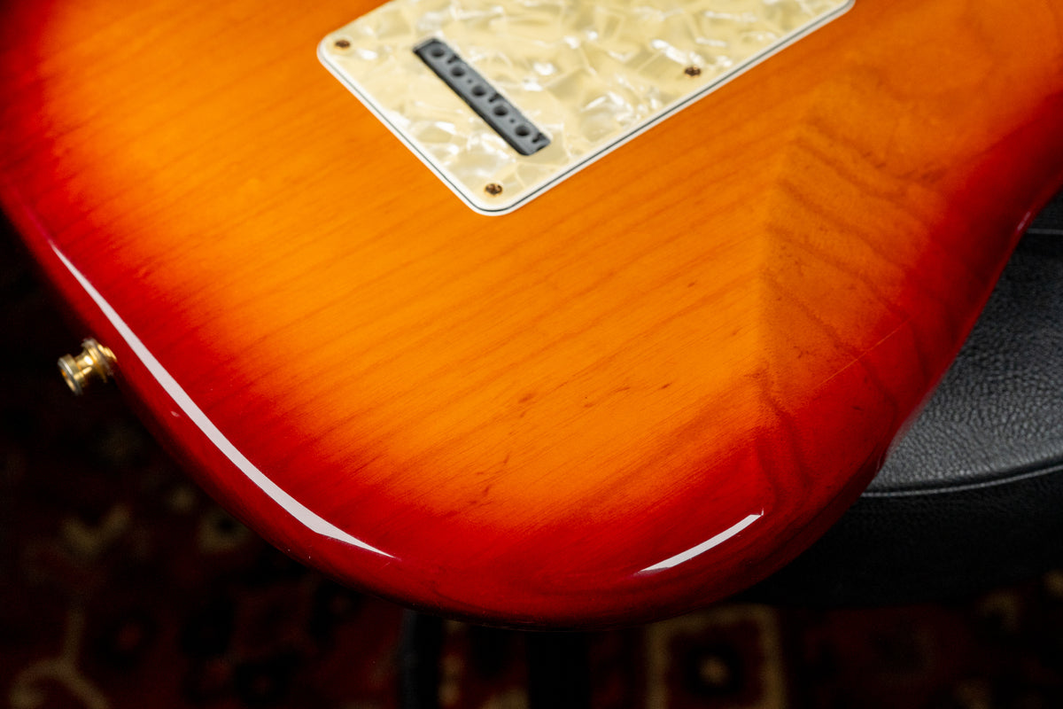Close-up of the guitar's lower body, showing a glossy sunburst finish with visible wood grain, a pearloid pickguard, and a gold strap button.
