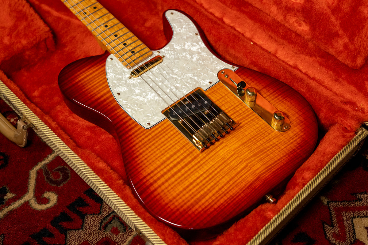 A flame top Telecaster in a sunburst finish with a pearloid pickguard and gold hardware, resting in a red velvet-lined case.