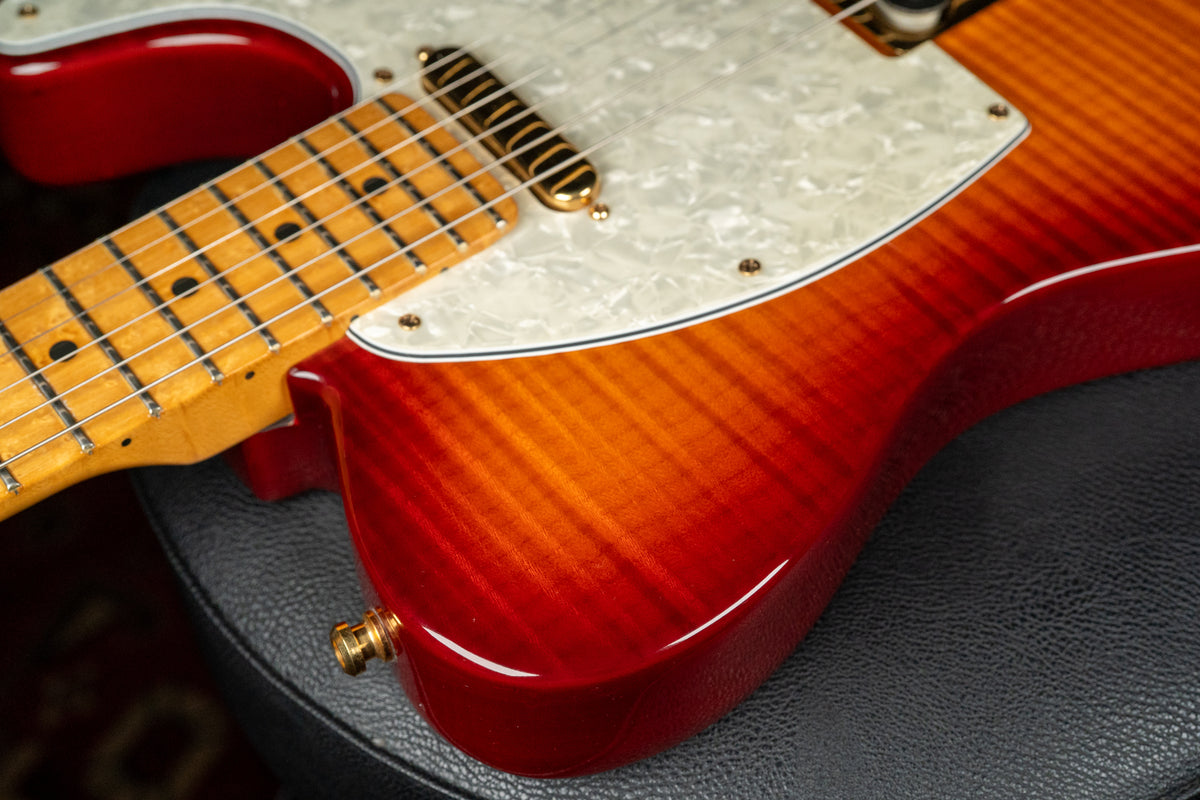 Close-up of the guitar's lower body, showing the flame top's red-orange burst, pearloid pickguard, and gold hardware.
