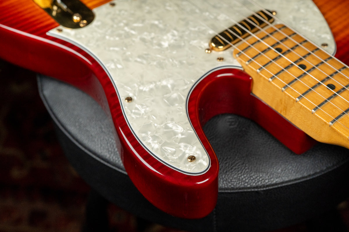 The lower bout of a red-to-orange sunburst Telecaster with a pearloid pickguard, gold hardware, and a maple neck.