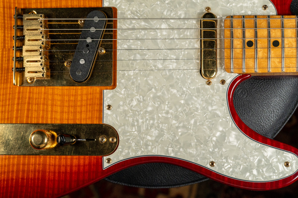Close-up of the guitar's lower body, showing a flame maple sunburst finish, gold hardware, and a pearloid pickguard with red trim.