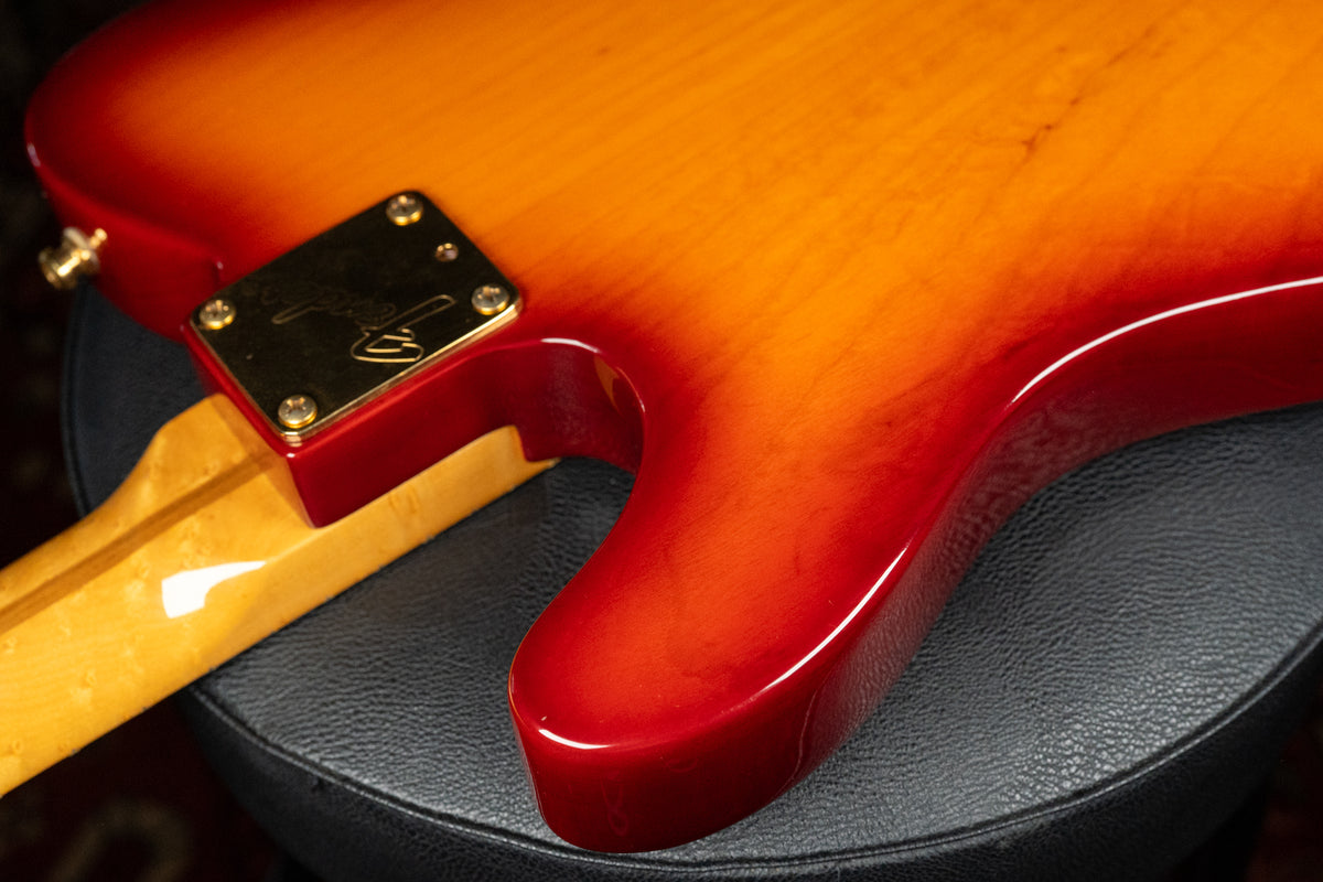 The guitar's lower bout and neck heel are visible, showing a glossy cherry sunburst finish and a gold neck plate.