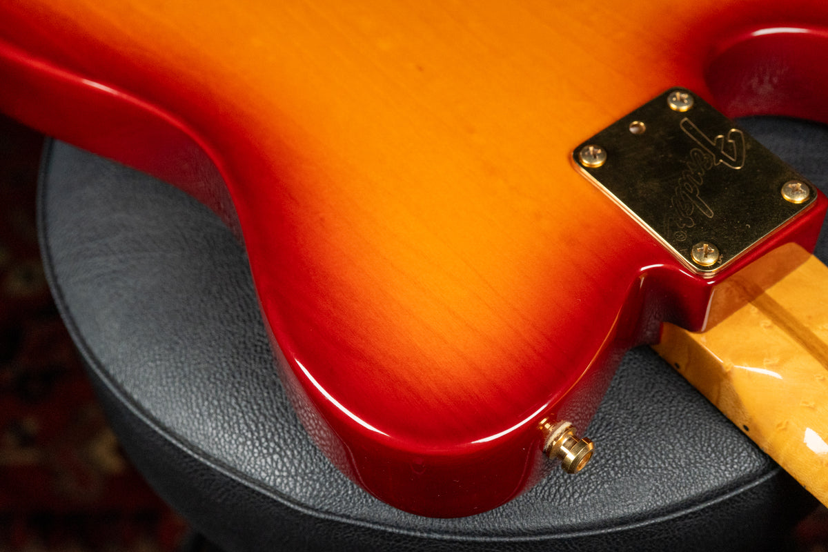 The guitar's lower body, in a glossy red-to-orange sunburst, shows a gold neck plate and strap button, with a light wood neck.