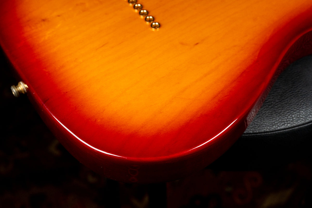 Close-up of the guitar's lower bout, showing a glossy sunburst finish with a gold strap button and six string-through-body ferrules.