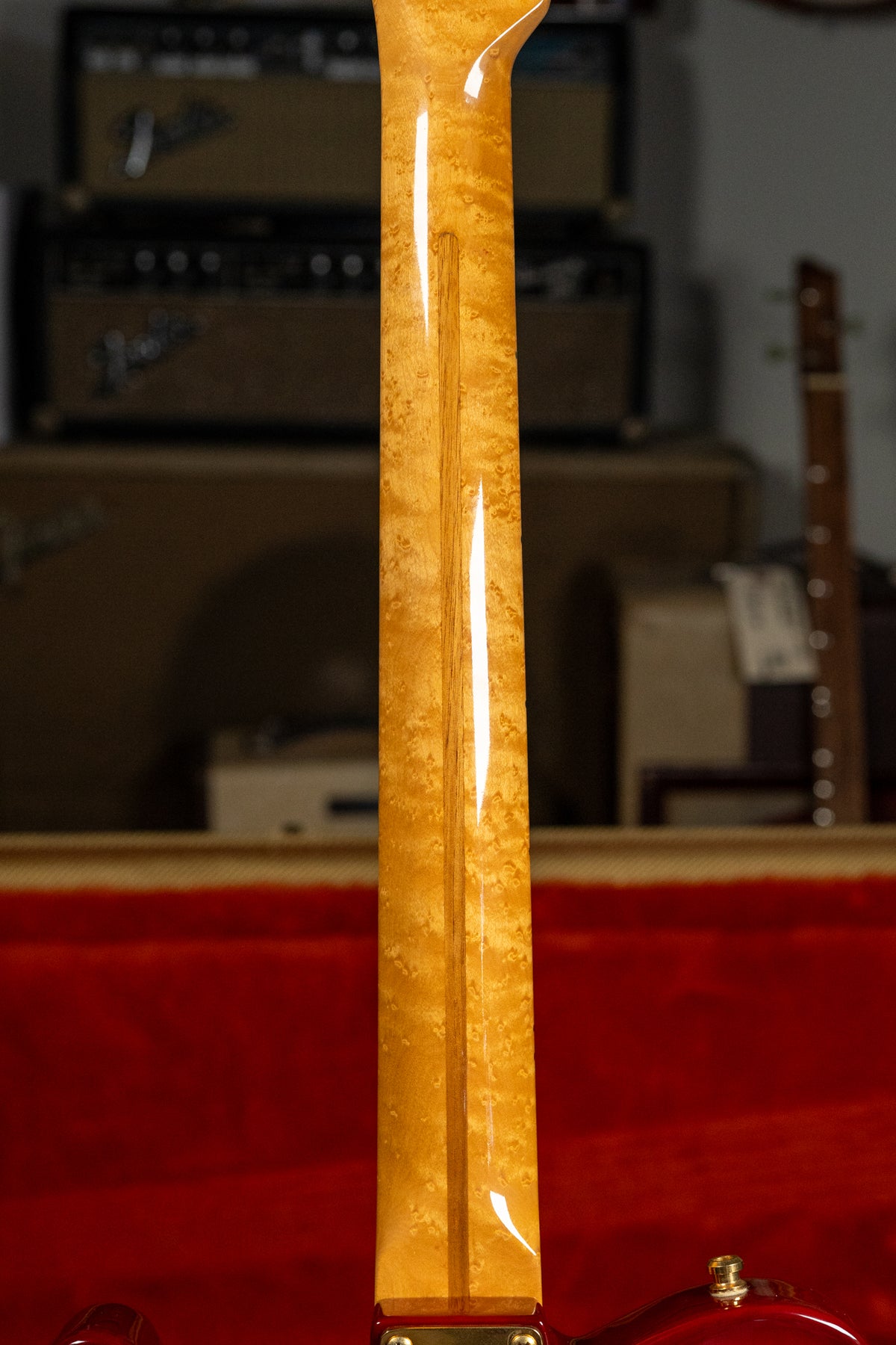 The back of a glossy, light-brown figured maple neck with a dark stripe down the center, meeting a red guitar body.