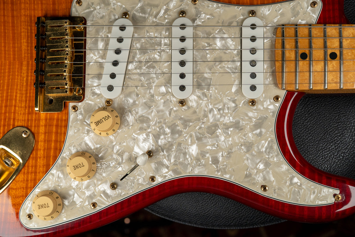 Close-up of a Stratocaster's body, showing a gold tremolo, three white single-coil pickups on a pearloid pickguard, and three cream knobs.