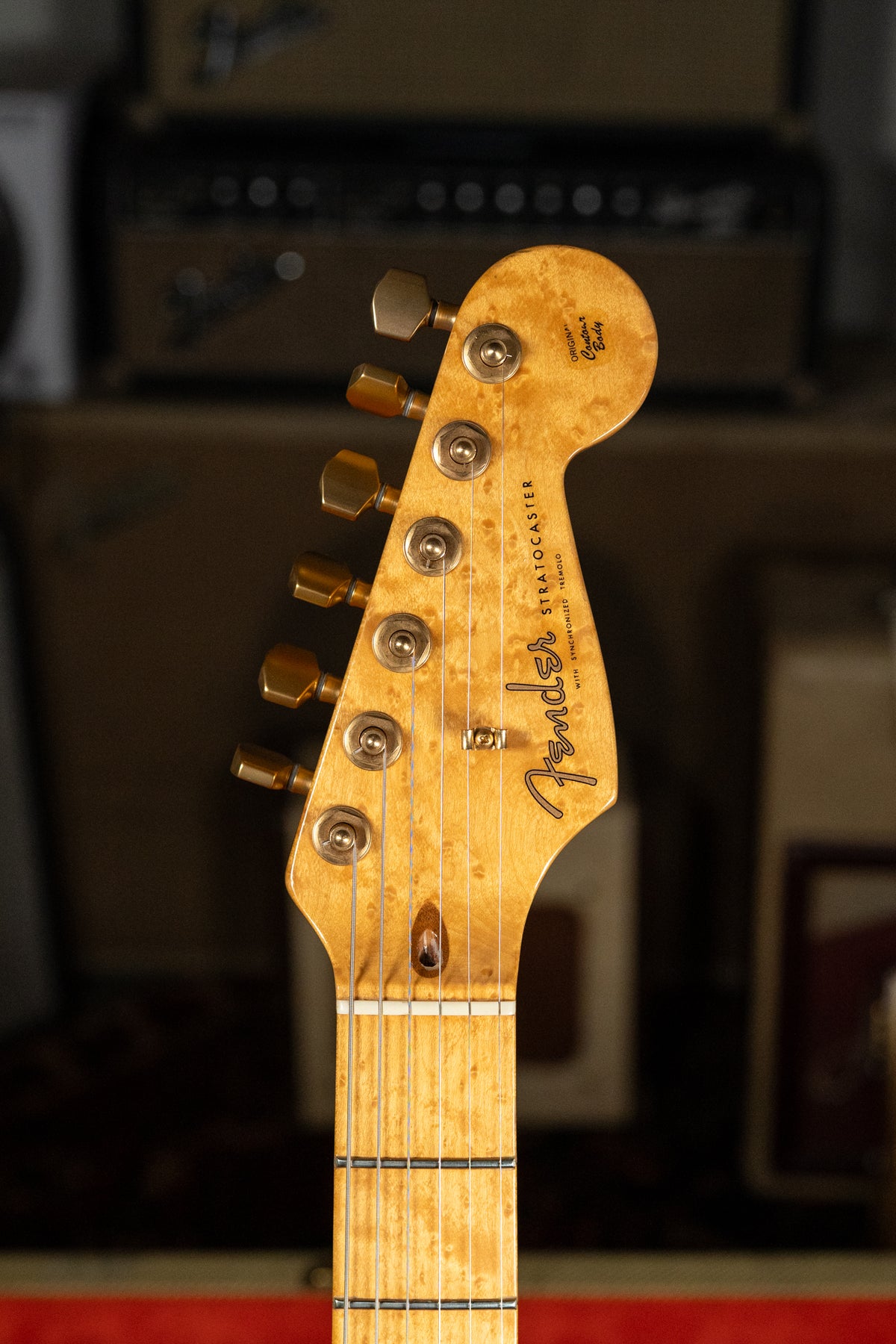 Close-up of a Stratocaster headstock and upper fretboard, showing a light wood with prominent grain and gold tuners.